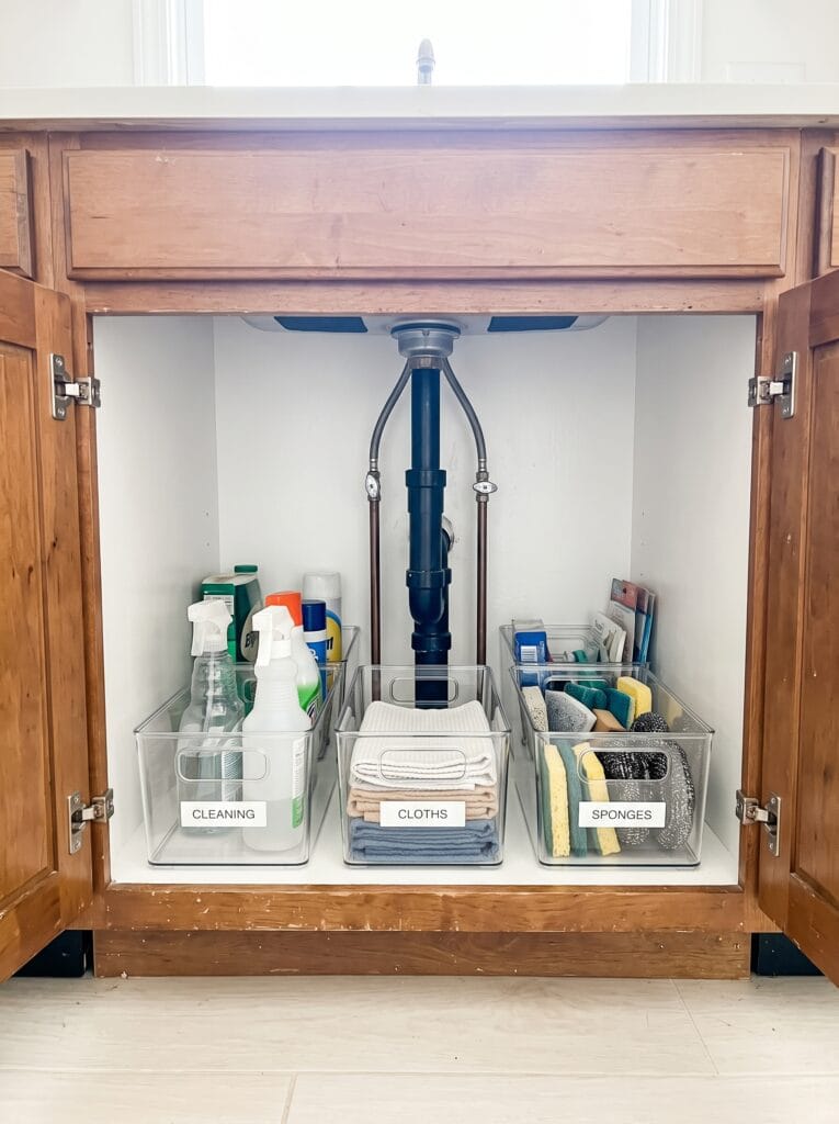Finished under sink cabinet with three clear labelled bins reading cleaning, cloths and sponges