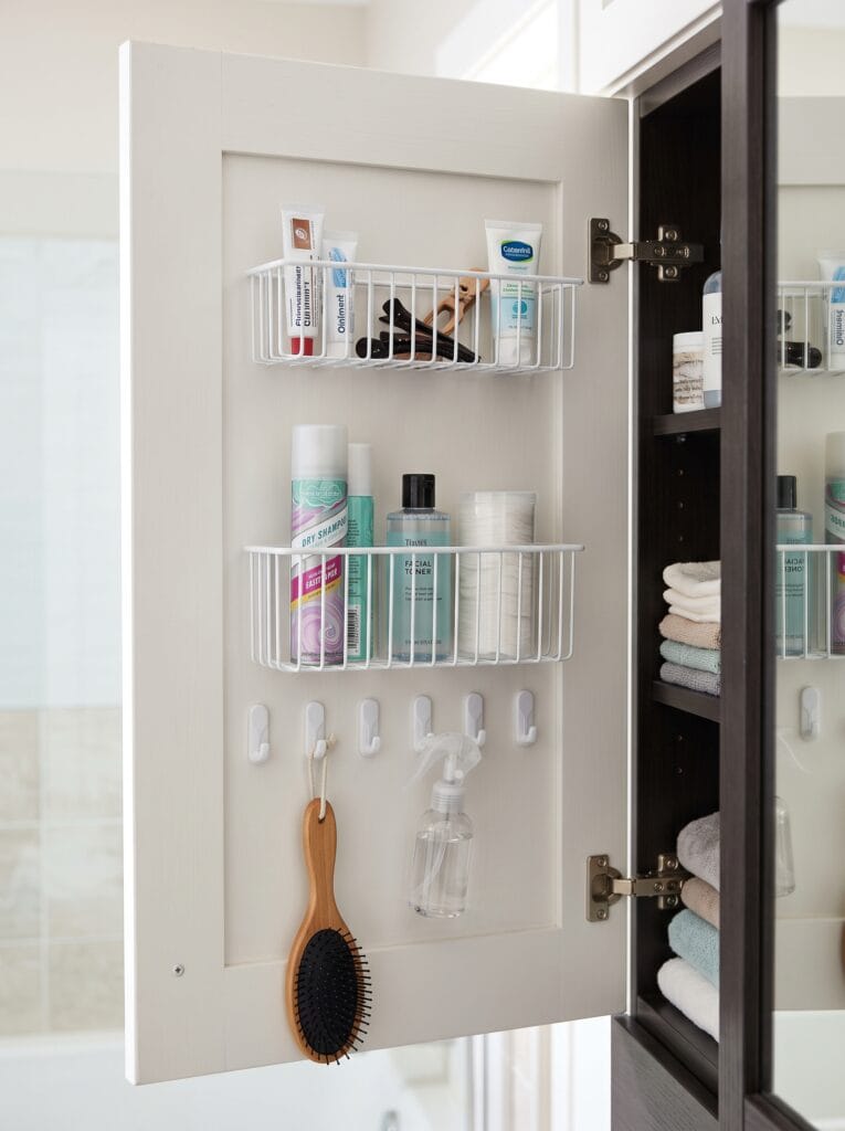 Inside of a cabinet door fitted with two white wire baskets and adhesive hooks