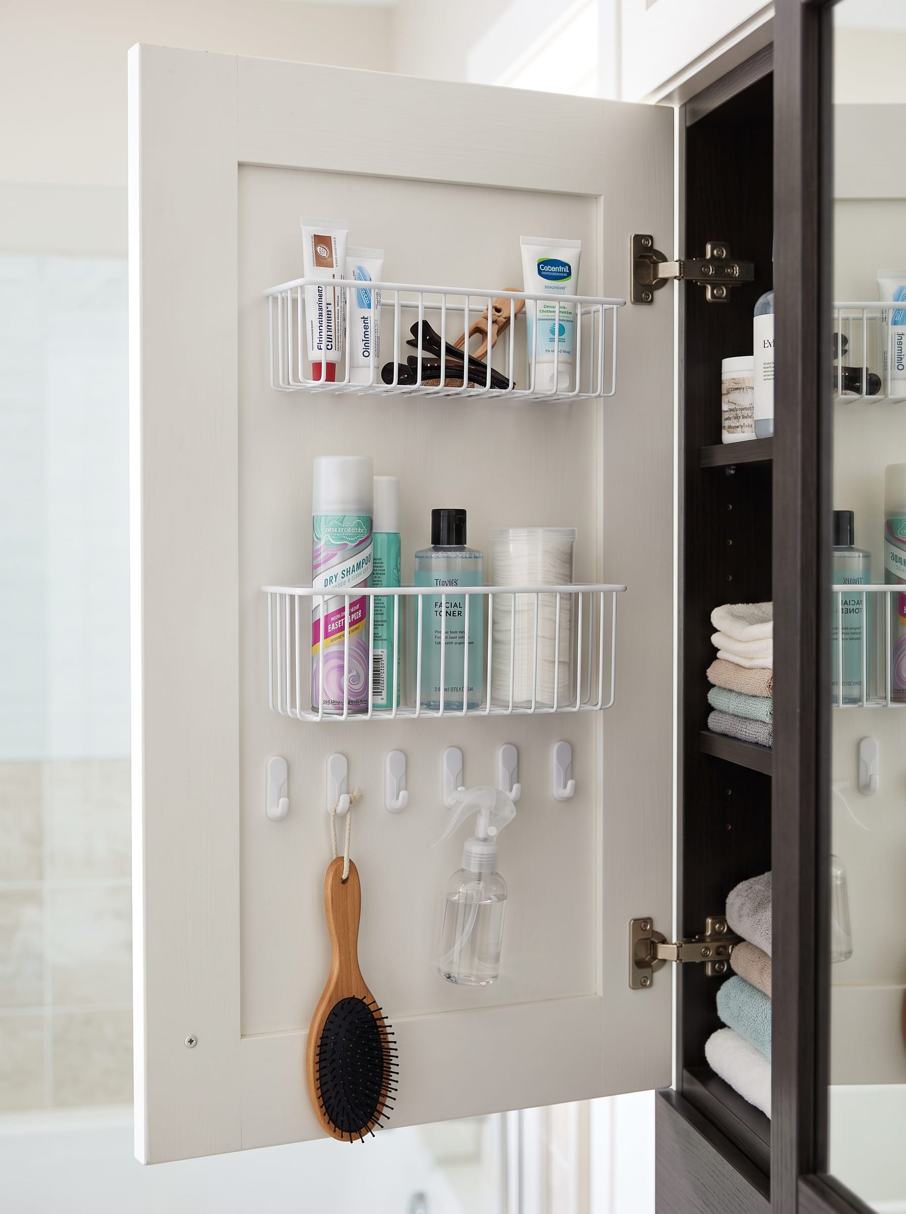 Inside of a cabinet door fitted with two white wire baskets and adhesive hooks