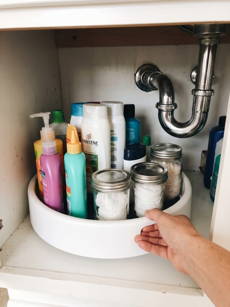 White turntable inside an under sink cabinet holding tall bottles with a hand turning it
