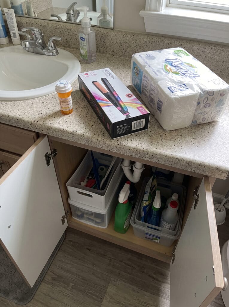 Medicine bottle, boxed hair straightener and a pack of paper goods set aside on a bathroom counter