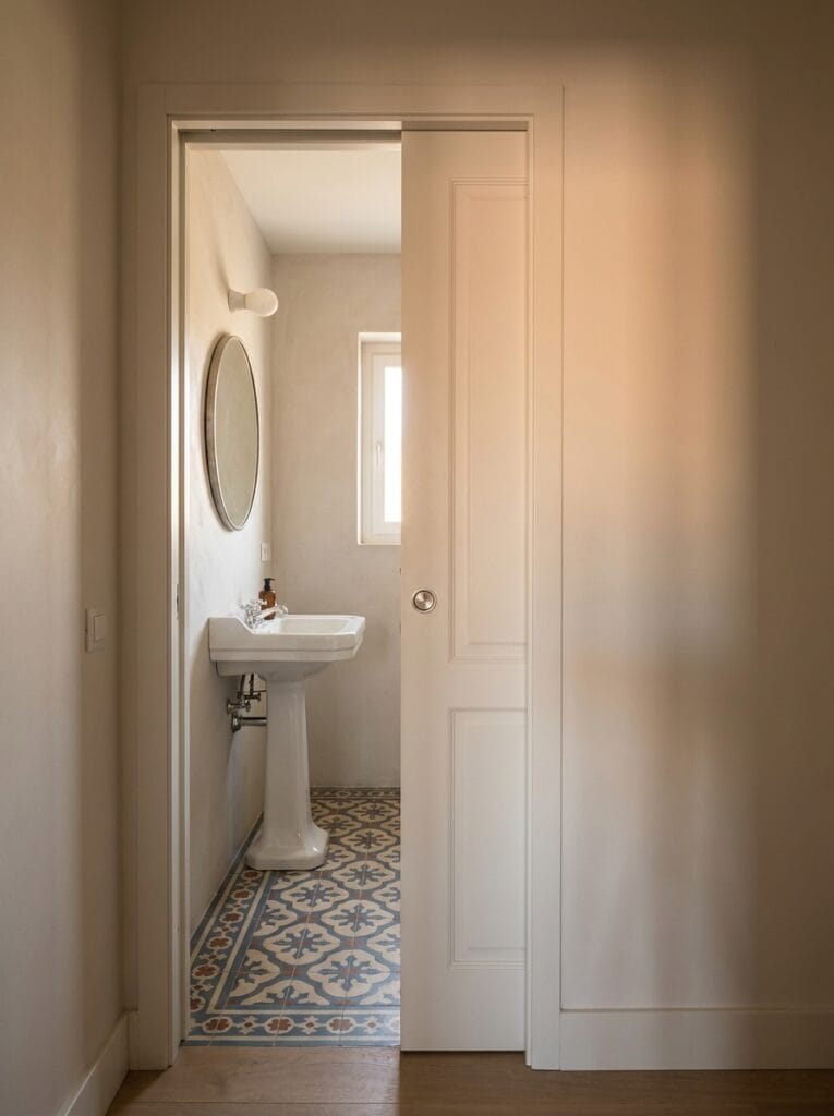 Pocket door slid halfway into the wall of a small bathroom with a pedestal sink and patterned floor