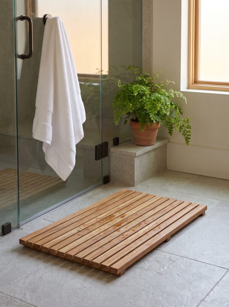 A solid teak slatted bath mat with water droplets in front of a glass shower door
