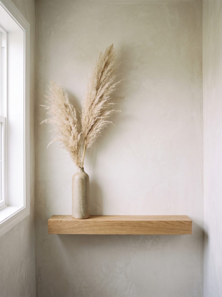 single oak shelf holding one tall stoneware vase with dried pampas grass on a plaster wall
