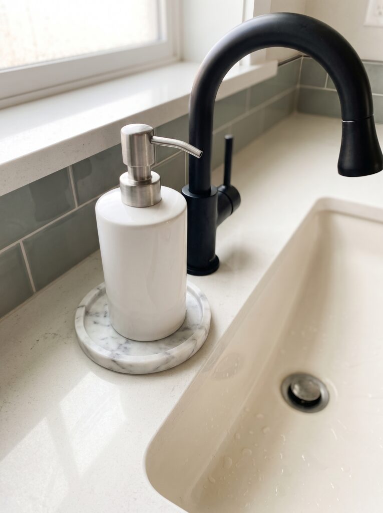 white ceramic soap pump on a marble coaster beside a black faucet and a cream basin with water droplets