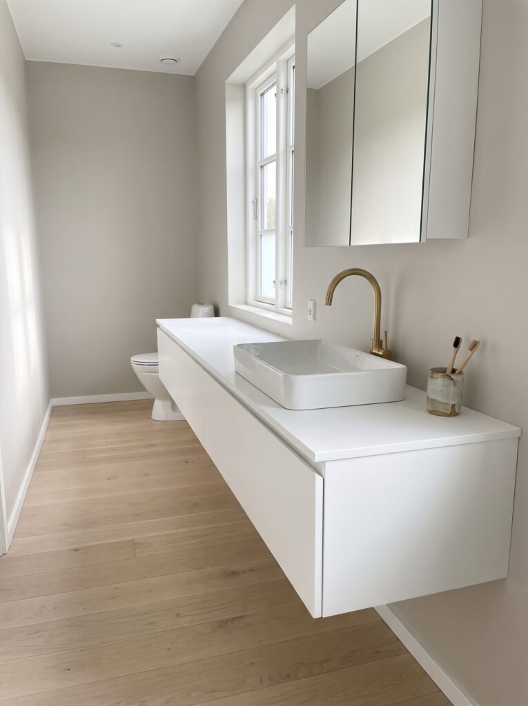 long white floating vanity with a toothbrush cup at the near end and the toilet at the far end of the room