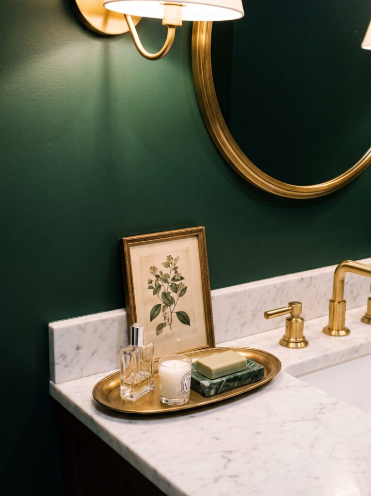 Aged brass oval tray with a perfume bottle, candle and green marble soap dish on a marble vanity