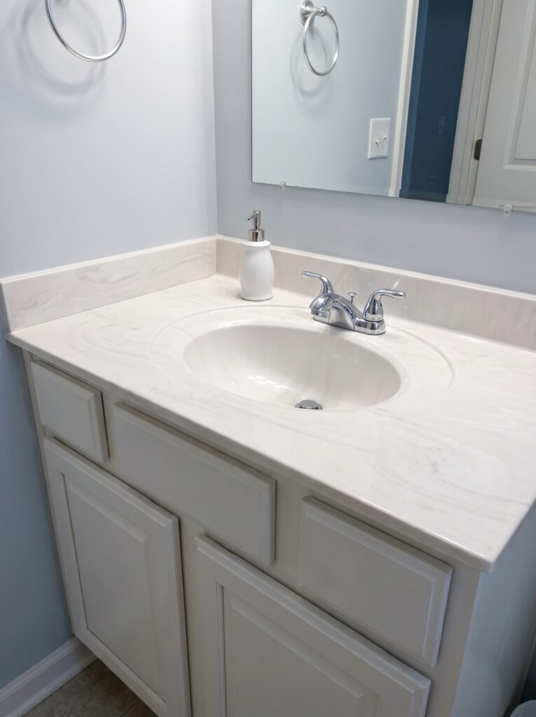 A cultured marble vanity top with an integrated oval basin, chrome faucet and soap pump on a white builder-style vanity