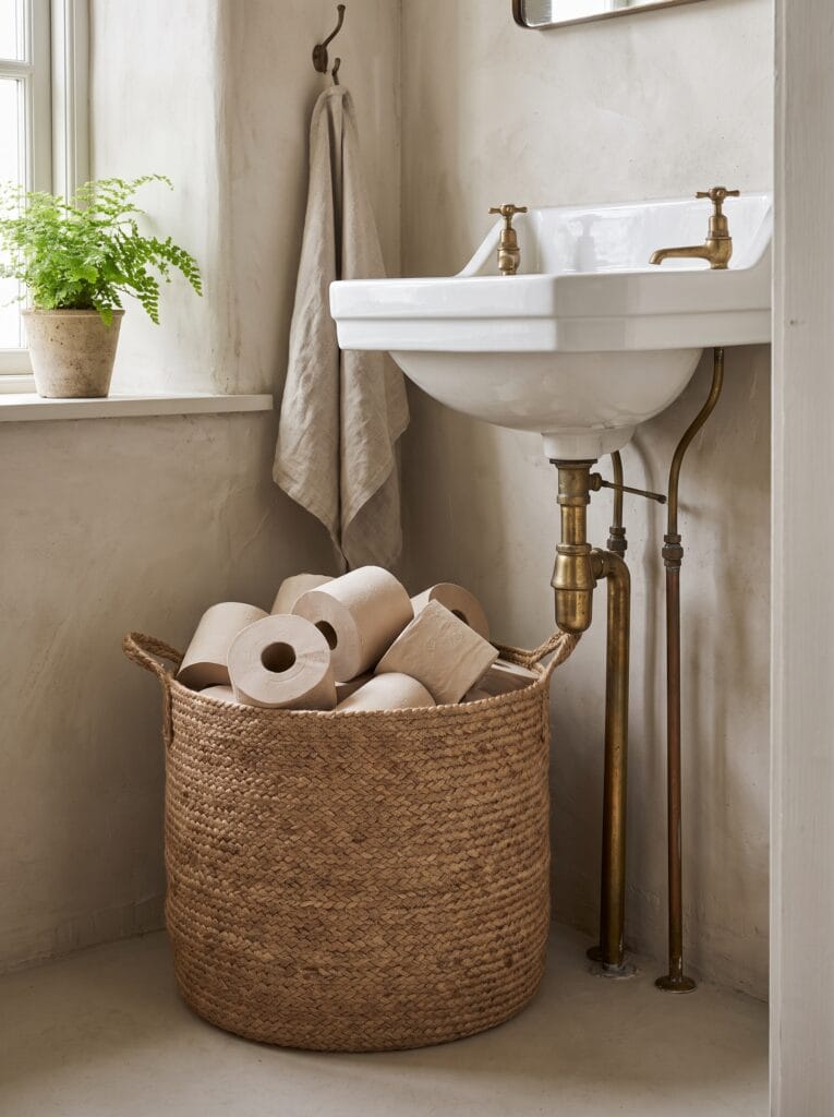 tall slim rattan basket beside a toilet holding magazines and rolled towels