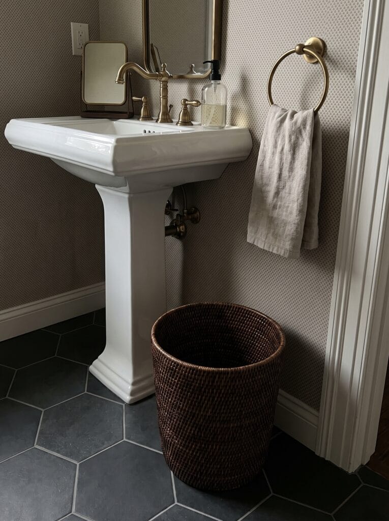 oval seagrass basket on a marble counter holding folded washcloths and a reed diffuser