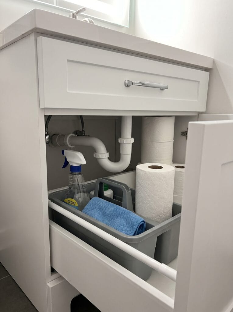 White under sink pull out drawer holding a grey caddy with a spray bottle microfiber cloth and paper towel rolls