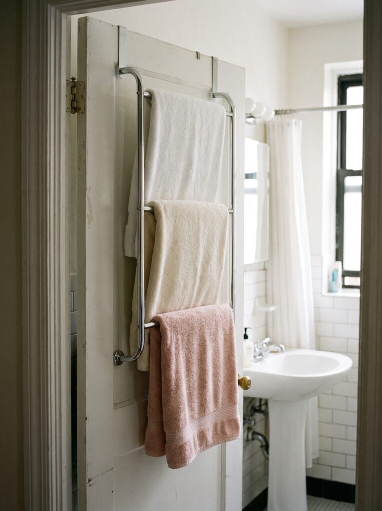 chrome three-tier over-the-door towel rack holding folded white, cream, and blush pink towels
