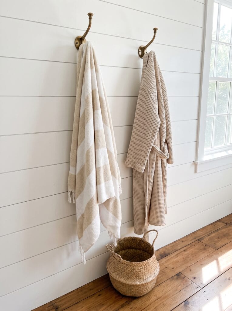 brass wall hooks holding a striped towel and waffle robe over a woven basket