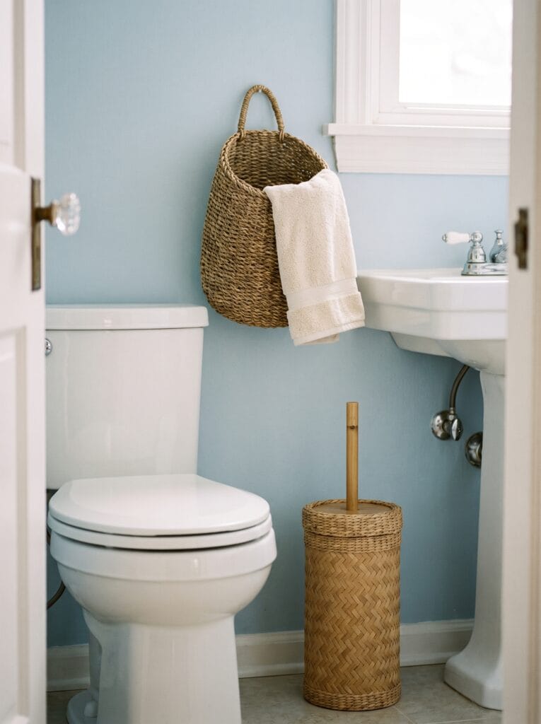 bamboo toilet brush holder beside a hanging woven towel basket in a pale blue powder room