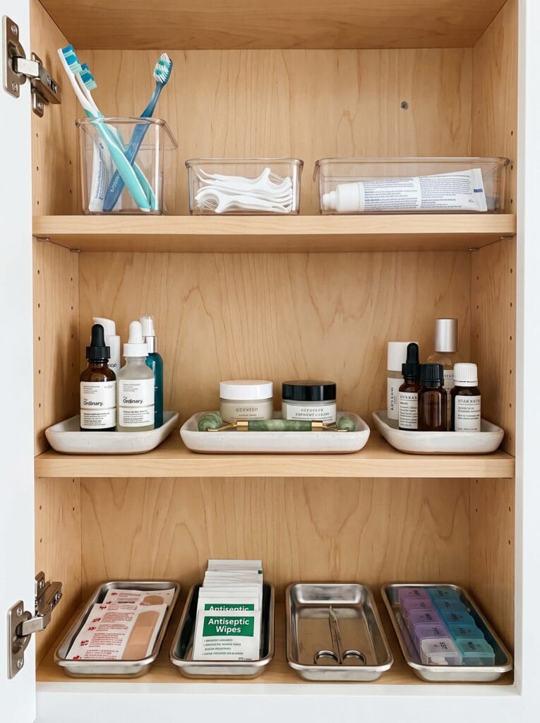 medicine cabinet shelves organized with a toothbrush cup, floss, skincare trays, and first aid and pill organizer trays