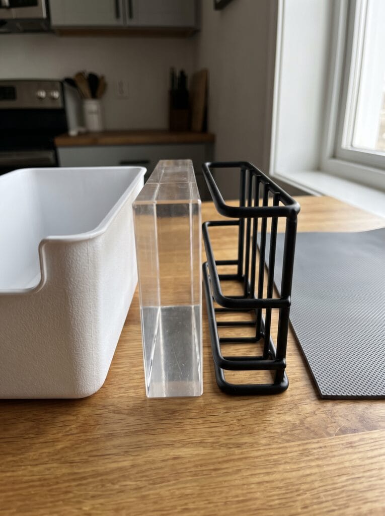 plastic bin, acrylic riser, wire rack, and rubber cabinet liner mat compared side by side on a counter